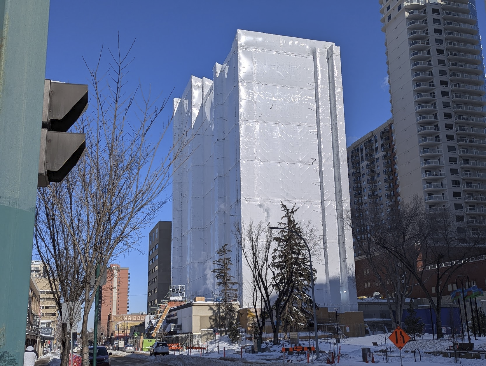 A photo of a highrise building completely wrapped in white plastic (while undergoing renovations) on a cold winter day.