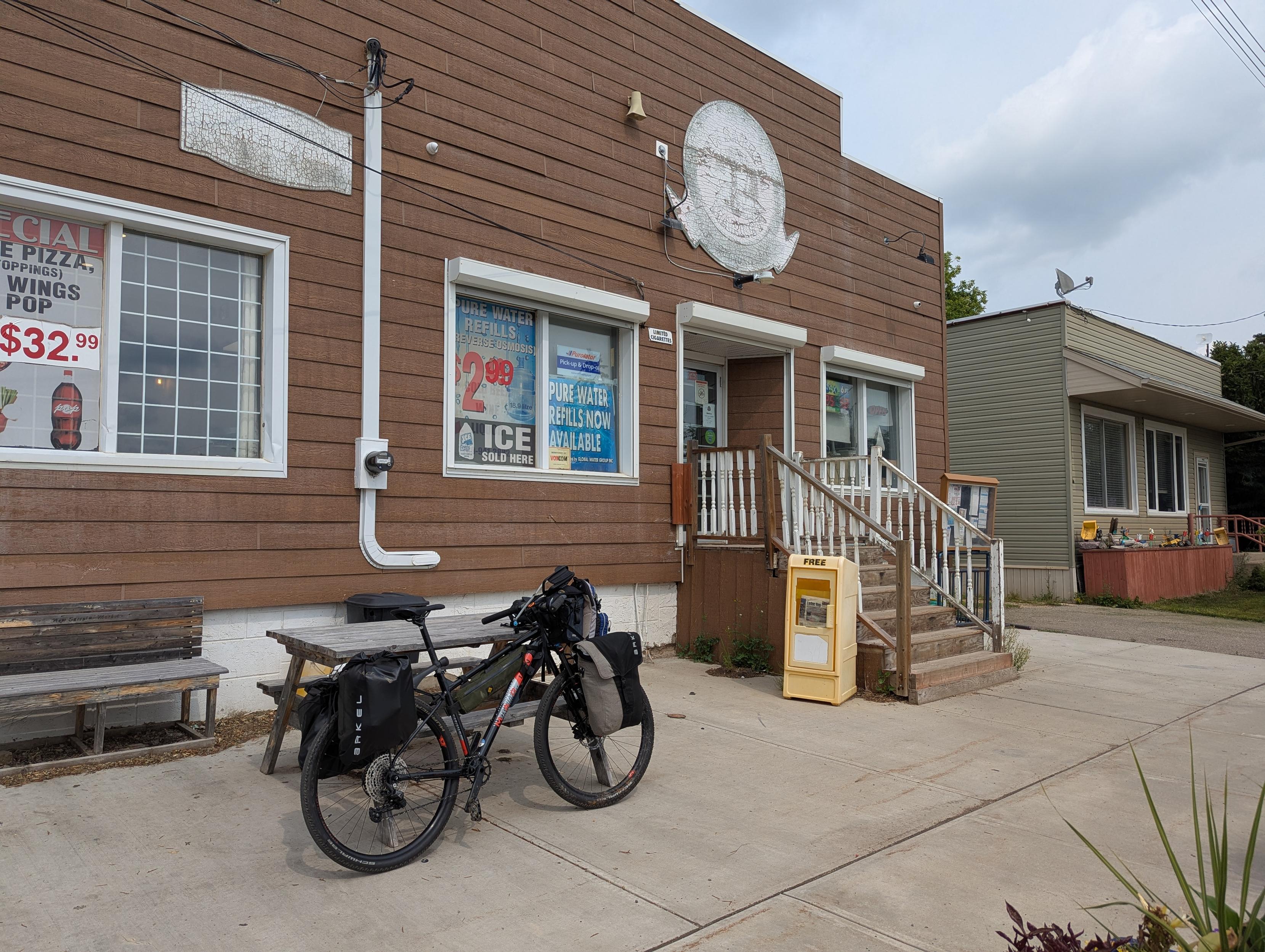 A laden mountain bike resting against a picnic table outside a small town general store.